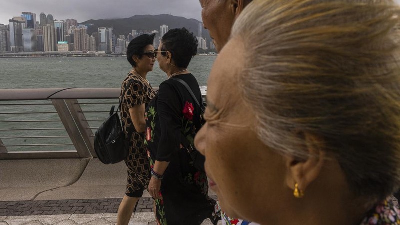Mainland Chinese tourists run along a promenade during a typhoon in Hong Kong, Monday, July 17, 2023. Schools and the stock market were closed in Hong Kong on Monday as Typhoon Talim swept south of the city. (AP Photo/Louise Delmotte)