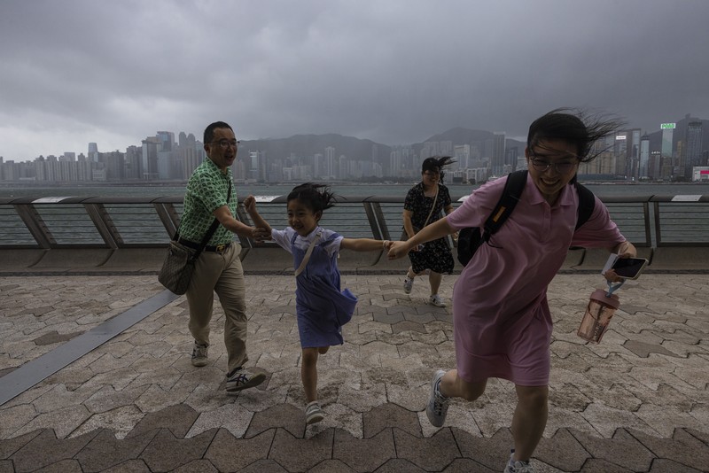 Hong Kong Typhoon Mainland Chinese tourists run along a promenade during a typhoon in Hong Kong, Monday, July 17, 2023. Schools and the stock market were closed in Hong Kong on Monday as Typhoon Talim swept south of the city. (AP Photo/Louise Delmotte)
