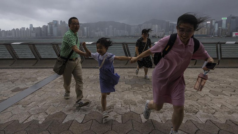 Mainland Chinese tourists run along a promenade during a typhoon in Hong Kong, Monday, July 17, 2023. Schools and the stock market were closed in Hong Kong on Monday as Typhoon Talim swept south of the city. (AP Photo/Louise Delmotte)