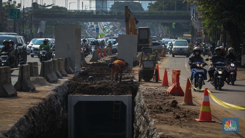 Pengendara melintas di dekat proyek pembangunan saluran air atau drainase di Jalan KH Abdullah Syafei, Jakarta, Senin (17/7/2023). (CNBC Indonesia/Faisal Rahman)