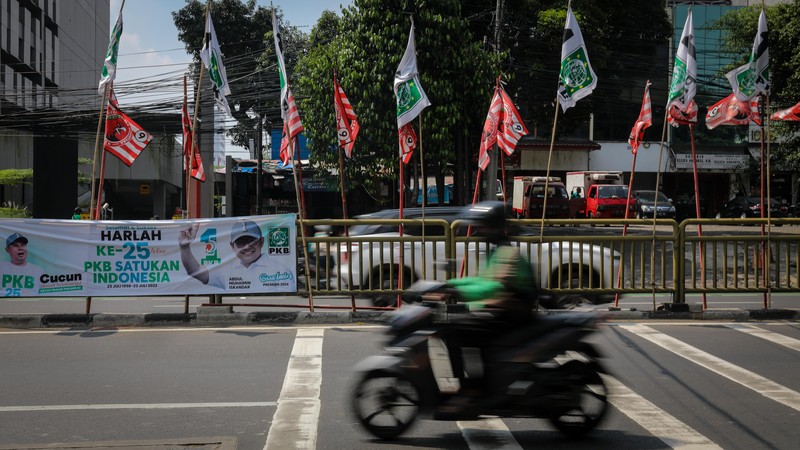 Pengendara melintas di dekat bendera parpol yang terpasang pada pembatas jalan di Jakarta, Selasa (18/7/2023).  (CNBC Indonesia/Faisal Rahman)