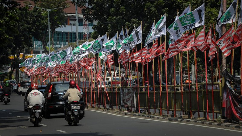 Pengendara melintas di dekat bendera parpol yang terpasang pada pembatas jalan di Jakarta, Selasa (18/7/2023).  (CNBC Indonesia/Faisal Rahman)