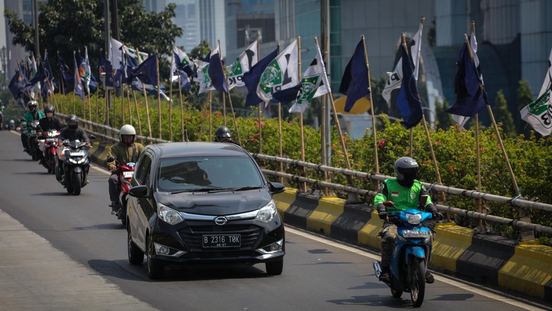 Pengendara melintas di dekat bendera parpol yang terpasang pada pembatas jalan di Jakarta, Selasa (18/7/2023).  (CNBC Indonesia/Faisal Rahman)