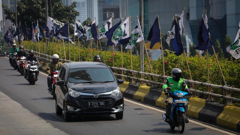 Pengendara melintas di dekat bendera parpol yang terpasang pada pembatas jalan di Jakarta, Selasa (18/7/2023).  (CNBC Indonesia/Faisal Rahman)
