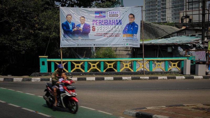 Pengendara melintas di dekat bendera parpol yang terpasang pada pembatas jalan di Jakarta, Selasa (18/7/2023).  (CNBC Indonesia/Faisal Rahman)