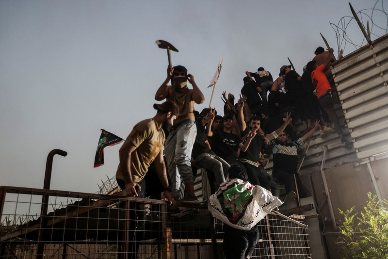 A protester holds up a portrait of Iraqi Shi'ite cleric Moqtada al-Sadr as smoke rises from the Swedish embassy building during a protest near the embassy, hours after it was stormed and set on fire ahead of an expected Koran burning in Stockholm, in Baghdad, Iraq, July 20, 2023. REUTERS/Ahmed Saad