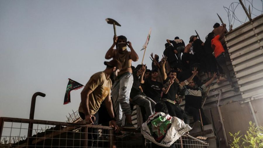 A protester holds up a portrait of Iraqi Shi'ite cleric Moqtada al-Sadr as smoke rises from the Swedish embassy building during a protest near the embassy, hours after it was stormed and set on fire ahead of an expected Koran burning in Stockholm, in Baghdad, Iraq, July 20, 2023. REUTERS/Ahmed Saad