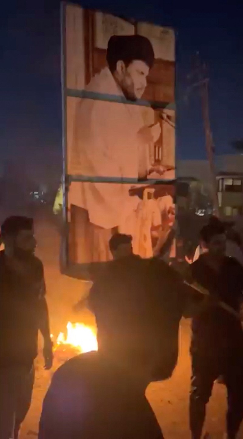 A protester holds up a portrait of Iraqi Shi'ite cleric Moqtada al-Sadr as smoke rises from the Swedish embassy building during a protest near the embassy, hours after it was stormed and set on fire ahead of an expected Koran burning in Stockholm, in Baghdad, Iraq, July 20, 2023. REUTERS/Ahmed Saad