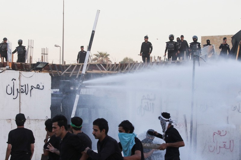 A protester holds up a portrait of Iraqi Shi'ite cleric Moqtada al-Sadr as smoke rises from the Swedish embassy building during a protest near the embassy, hours after it was stormed and set on fire ahead of an expected Koran burning in Stockholm, in Baghdad, Iraq, July 20, 2023. REUTERS/Ahmed Saad