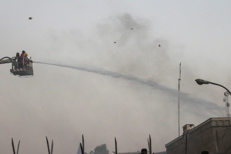 A protester holds up a portrait of Iraqi Shi'ite cleric Moqtada al-Sadr as smoke rises from the Swedish embassy building during a protest near the embassy, hours after it was stormed and set on fire ahead of an expected Koran burning in Stockholm, in Baghdad, Iraq, July 20, 2023. REUTERS/Ahmed Saad