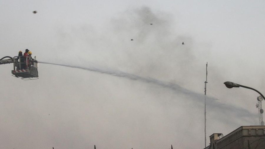 A protester holds up a portrait of Iraqi Shi'ite cleric Moqtada al-Sadr as smoke rises from the Swedish embassy building during a protest near the embassy, hours after it was stormed and set on fire ahead of an expected Koran burning in Stockholm, in Baghdad, Iraq, July 20, 2023. REUTERS/Ahmed Saad