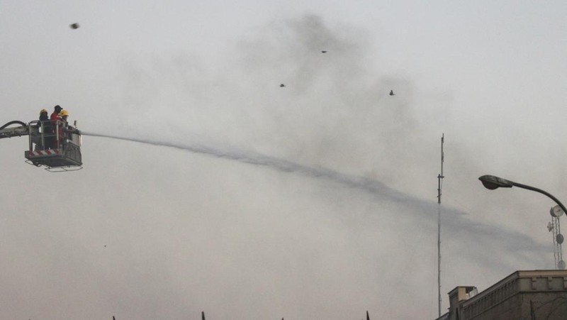 A protester holds up a portrait of Iraqi Shi'ite cleric Moqtada al-Sadr as smoke rises from the Swedish embassy building during a protest near the embassy, hours after it was stormed and set on fire ahead of an expected Koran burning in Stockholm, in Baghdad, Iraq, July 20, 2023. REUTERS/Ahmed Saad