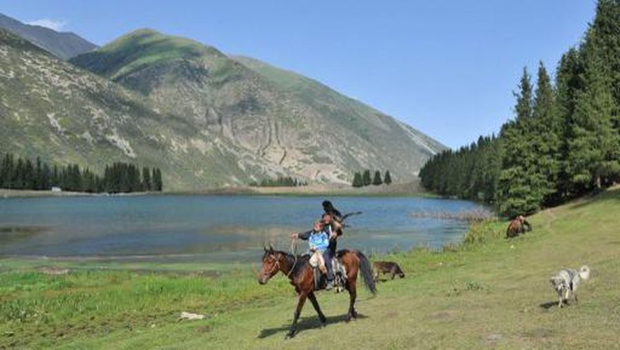 Holding his hunting bird of prey a Kyrgyz man rides a horse together with a young tourist near the Kara-Kul lake on the Chon-Ak-Suu valley close to the famous Issyk-Kul lake, some 300 km southeast of Bishkek, the capital of Kyrgyzstan, on July 22, 2014. AFP PHOTO / VYACHESLAV OSELEDKO (Photo by VYACHESLAV OSELEDKO / AFP)