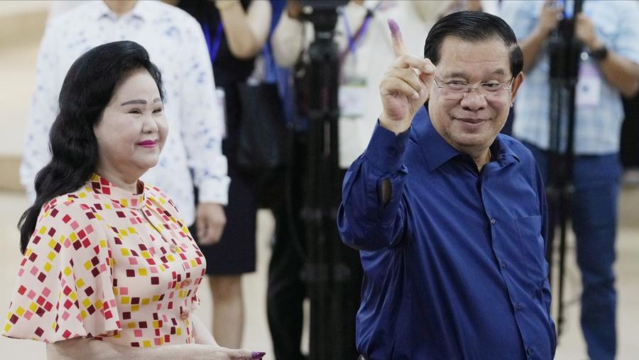 Perdana Menteri Kamboja Hun Sen, kanan, dari Partai Rakyat Kamboja (CPP) memamerkan jarinya yang bertinta, berdiri di samping istrinya Bun Rany, kiri, setelah memberikan suara di sebuah tempat pemungutan suara di Takhmua di provinsi Kandal, tenggara Phnom Penh, Kamboja, Minggu, 23 Juli 2023. (AP Photo/Heng Sinith)