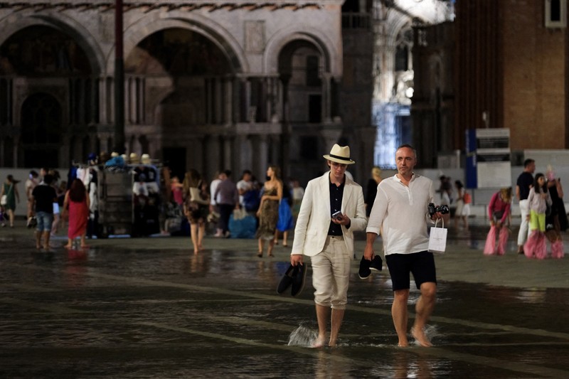 Turis bejalan saat banjir merendam Alun-alun St Mark di kota Venesia, Italia, Selasa (1/8/2023) malam waktu setempat. (REUTERS/Manuel Silvestri)