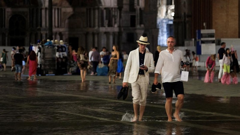 Turis bejalan saat banjir merendam Alun-alun St Mark di kota Venesia, Italia, Selasa (1/8/2023) malam waktu setempat. (REUTERS/Manuel Silvestri)