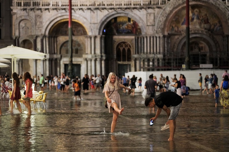 Turis bejalan saat banjir merendam Alun-alun St Mark di kota Venesia, Italia, Selasa (1/8/2023) malam waktu setempat. (REUTERS/Manuel Silvestri)