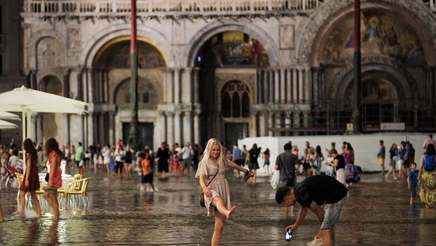 Turis bejalan saat banjir merendam Alun-alun St Mark di kota Venesia, Italia, Selasa (1/8/2023) malam waktu setempat. (REUTERS/Manuel Silvestri)