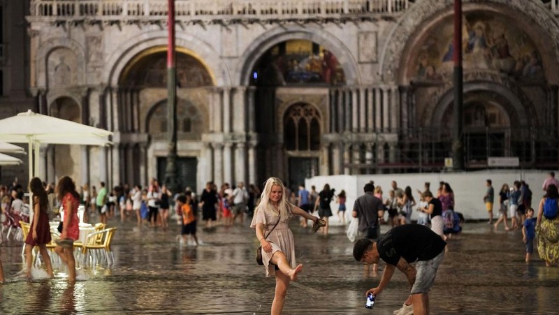 Turis bejalan saat banjir merendam Alun-alun St Mark di kota Venesia, Italia, Selasa (1/8/2023) malam waktu setempat. (REUTERS/Manuel Silvestri)