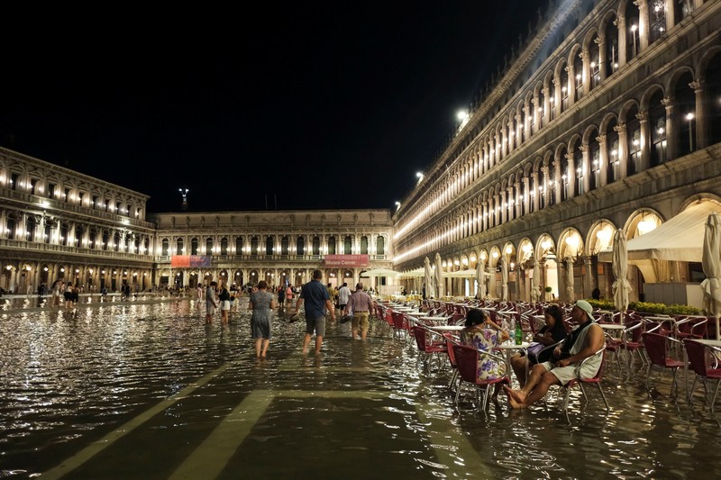 Turis bejalan saat banjir merendam Alun-alun St Mark di kota Venesia, Italia, Selasa (1/8/2023) malam waktu setempat. (REUTERS/Manuel Silvestri)
