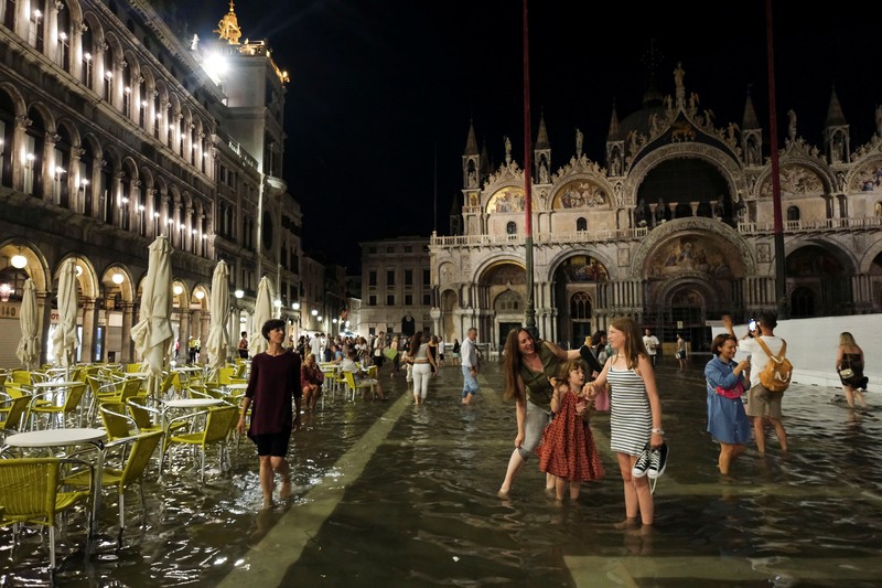 Turis bejalan saat banjir merendam Alun-alun St Mark di kota Venesia, Italia, Selasa (1/8/2023) malam waktu setempat. (REUTERS/Manuel Silvestri)