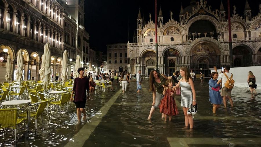 Turis bejalan saat banjir merendam Alun-alun St Mark di kota Venesia, Italia, Selasa (1/8/2023) malam waktu setempat. (REUTERS/Manuel Silvestri)