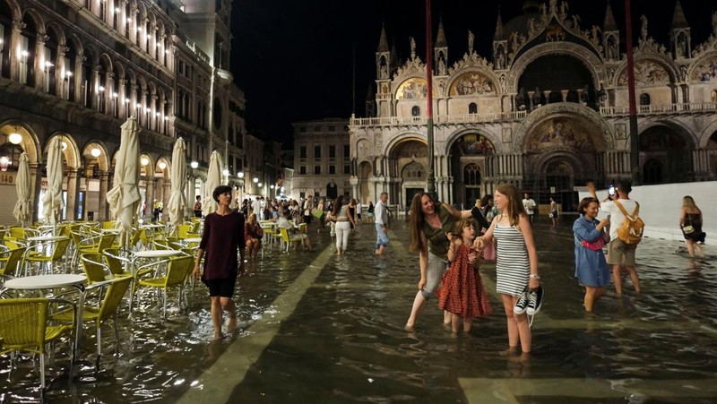 Turis bejalan saat banjir merendam Alun-alun St Mark di kota Venesia, Italia, Selasa (1/8/2023) malam waktu setempat. (REUTERS/Manuel Silvestri)