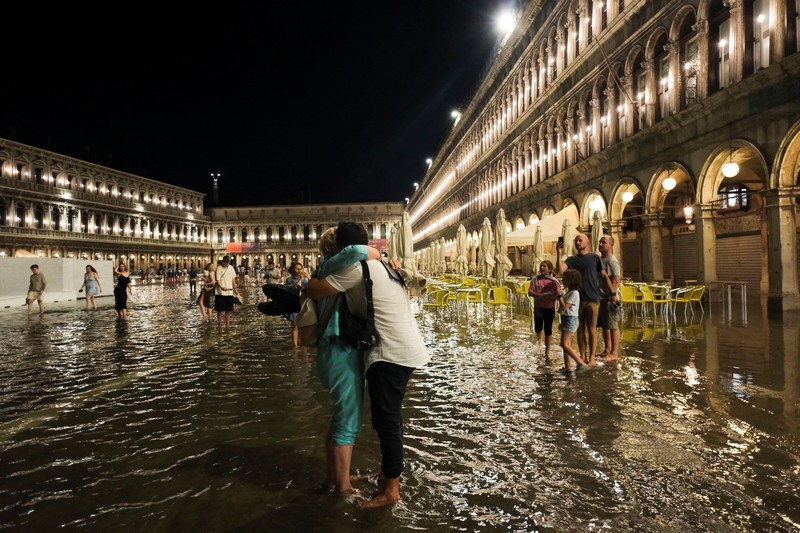 Turis bejalan saat banjir merendam Alun-alun St Mark di kota Venesia, Italia, Selasa (1/8/2023) malam waktu setempat. (REUTERS/Manuel Silvestri)