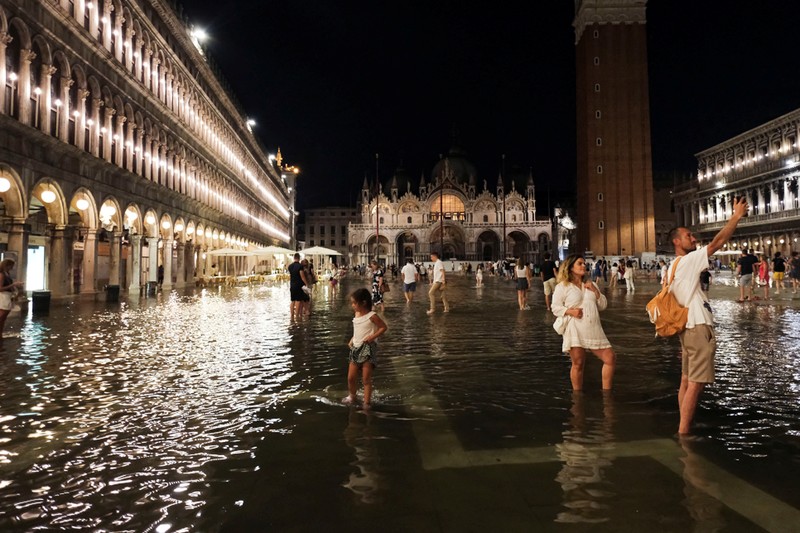 Turis bejalan saat banjir merendam Alun-alun St Mark di kota Venesia, Italia, Selasa (1/8/2023) malam waktu setempat. (REUTERS/Manuel Silvestri)