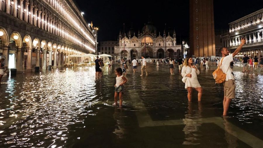Turis bejalan saat banjir merendam Alun-alun St Mark di kota Venesia, Italia, Selasa (1/8/2023) malam waktu setempat. (REUTERS/Manuel Silvestri)