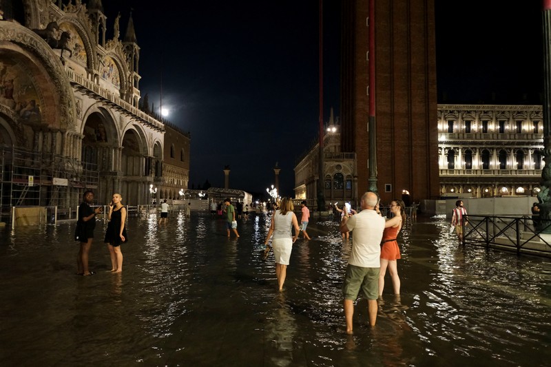 Turis bejalan saat banjir merendam Alun-alun St Mark di kota Venesia, Italia, Selasa (1/8/2023) malam waktu setempat. (REUTERS/Manuel Silvestri)