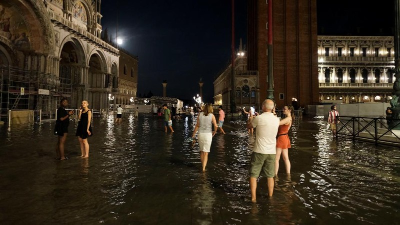 Turis bejalan saat banjir merendam Alun-alun St Mark di kota Venesia, Italia, Selasa (1/8/2023) malam waktu setempat. (REUTERS/Manuel Silvestri)