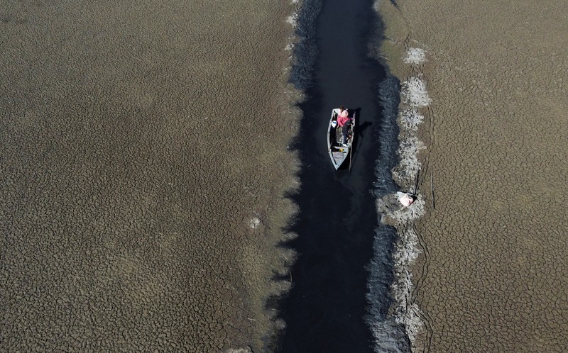 Isabel Apaza dan Gabriel Flores menaiki perahu mereka melalui jalur air sempit di dekat pantai Danau Titicaca pada musim kemarau di Huarina, Bolivia 3 Agustus 2023. (REUTERS/Claudia Morales)
