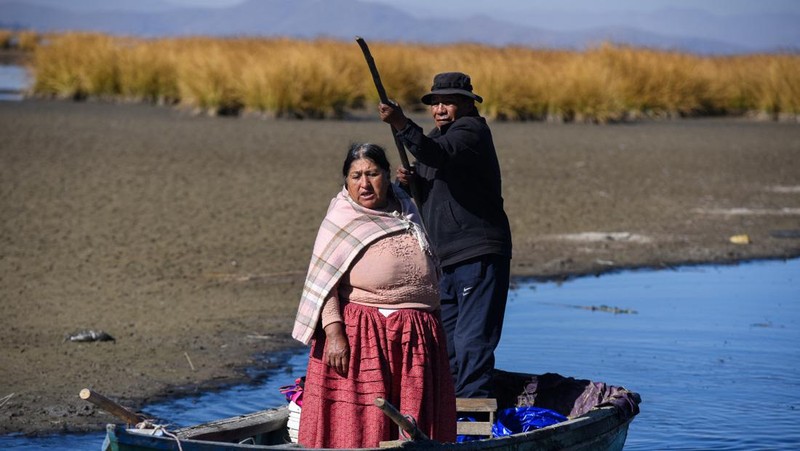 Isabel Apaza dan Gabriel Flores menaiki perahu mereka melalui jalur air sempit di dekat pantai Danau Titicaca pada musim kemarau di Huarina, Bolivia 3 Agustus 2023. (REUTERS/Claudia Morales)