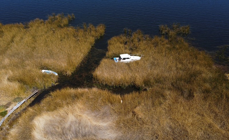 Isabel Apaza dan Gabriel Flores menaiki perahu mereka melalui jalur air sempit di dekat pantai Danau Titicaca pada musim kemarau di Huarina, Bolivia 3 Agustus 2023. (REUTERS/Claudia Morales)