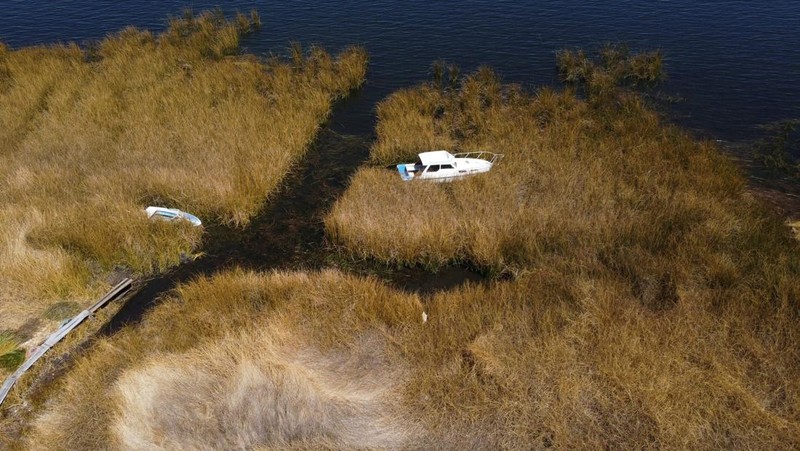 Isabel Apaza dan Gabriel Flores menaiki perahu mereka melalui jalur air sempit di dekat pantai Danau Titicaca pada musim kemarau di Huarina, Bolivia 3 Agustus 2023. (REUTERS/Claudia Morales)