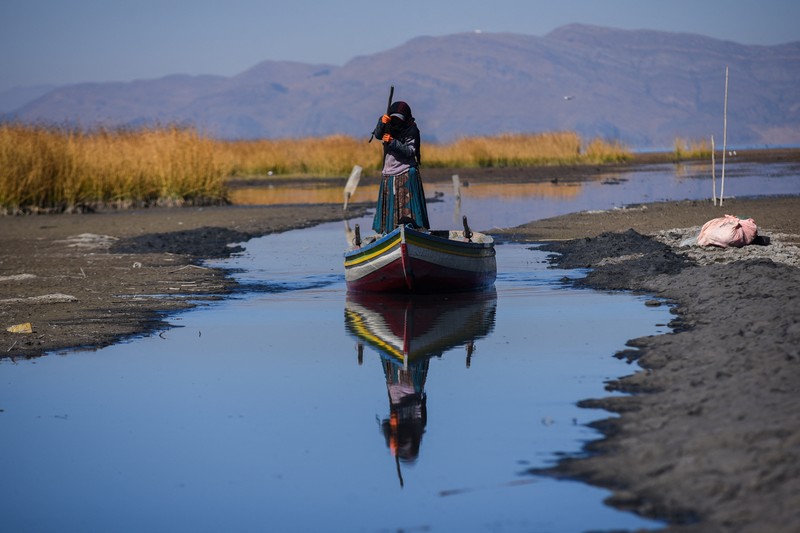 Isabel Apaza dan Gabriel Flores menaiki perahu mereka melalui jalur air sempit di dekat pantai Danau Titicaca pada musim kemarau di Huarina, Bolivia 3 Agustus 2023. (REUTERS/Claudia Morales)