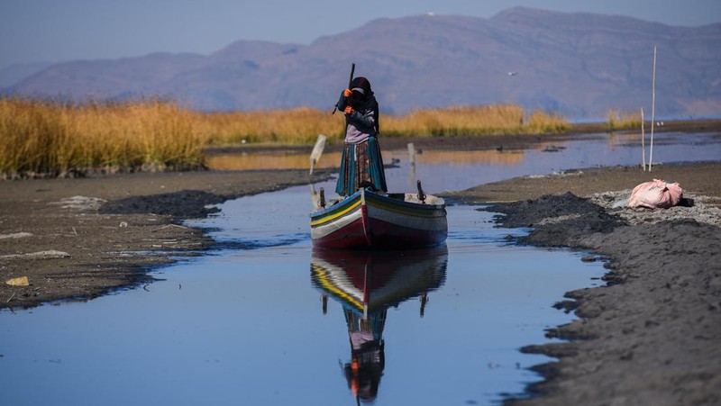 Isabel Apaza dan Gabriel Flores menaiki perahu mereka melalui jalur air sempit di dekat pantai Danau Titicaca pada musim kemarau di Huarina, Bolivia 3 Agustus 2023. (REUTERS/Claudia Morales)