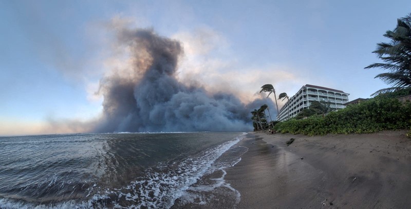 Orang-orang menyaksikan asap dan api memenuhi udara dari amukan kebakaran hutan di Front Street di pusat kota Lahaina, Maui pada Selasa, 8 Agustus 2023. Para pejabat Maui mengatakan kebakaran di kota bersejarah itu telah menghanguskan sebagian dari salah satu kawasan wisata paling populer di Hawaii. . Juru bicara County of Maui, Mahina Martin mengatakan dalam sebuah wawancara telepon pada Rabu pagi, kebakaran meluas di Lahaina, termasuk Front Street, area kota yang populer dengan turis. (Alan Dickar via AP)