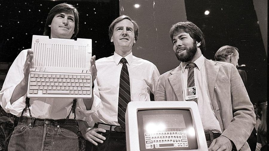 FILE - In this April 24, 1984 file photo, Steve Jobs, left, chairman of Apple Computers, John Sculley, center, president and CEO, and Steve Wozniak, co-founder of Apple, unveil the new Apple IIc computer in San Francisco. Steve Jobs, released Friday, Oct. 9, 2015, is the latest movie to examine a charismatic visionary who mesmerized the masses with his trendsetting gadgets while alienating his subordinates and friends with an almost-inhumane cruel streak. The story is told through Jobs interactions with six central figures in his life: his former marketing chief, Joanna Hoffman; his former girlfriend Chrisann Brennan; Apple co-founder and friend Wozniak; former Apple engineer Andy Hertzfeld; former Apple CEO Sculley; and Lisa, the daughter that Jobs refused to acknowledge for many years. (AP Photo/Sal Veder, File)