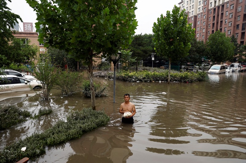 ASIA-WEATHER/CHINA-FLOODS FILE PHOTO: FILE PHOTO:A man holding a child walks across a damaged bridge after the rains and floods brought by remnants of Typhoon Doksuri, in Zhuozhou, Hebei province, China August 7, 2023. REUTERS/Tingshu Wang TPX IMAGES OF THE DAY/File Photo