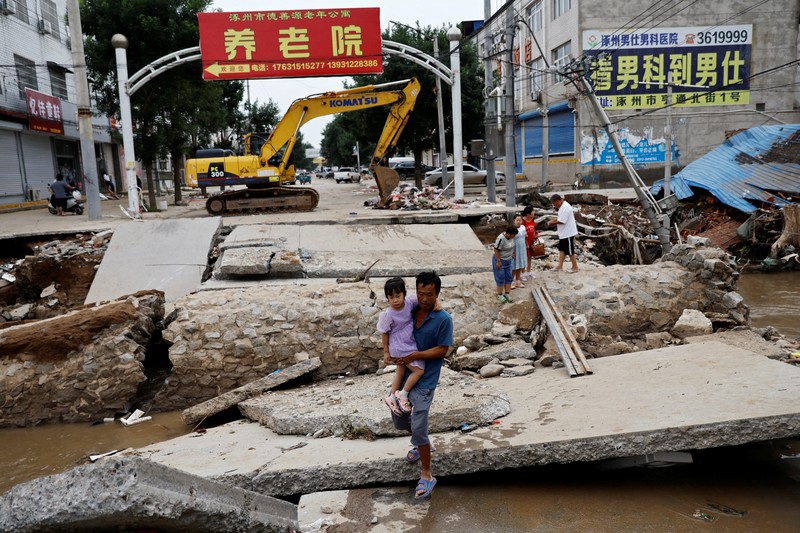 FILE PHOTO: FILE PHOTO:A man holding a child walks across a damaged bridge after the rains and floods brought by remnants of Typhoon Doksuri, in Zhuozhou, Hebei province, China August 7, 2023. REUTERS/Tingshu Wang     TPX IMAGES OF THE DAY/File Photo