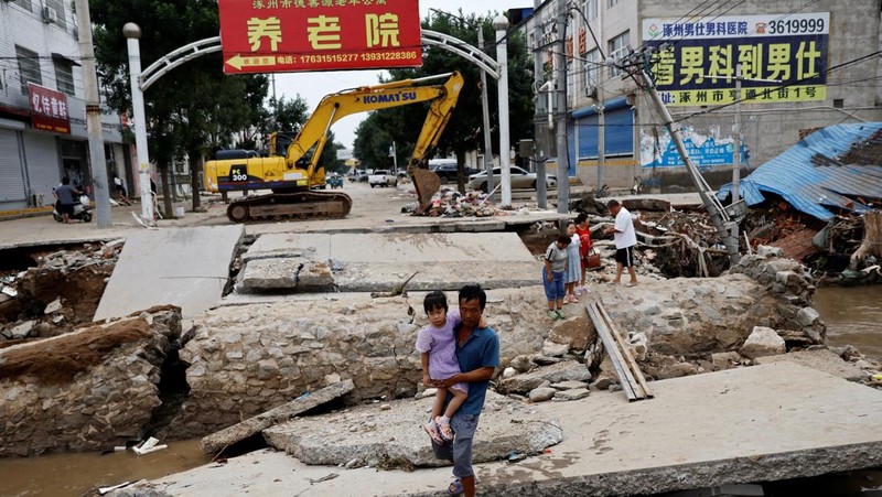 FILE PHOTO: FILE PHOTO:A man holding a child walks across a damaged bridge after the rains and floods brought by remnants of Typhoon Doksuri, in Zhuozhou, Hebei province, China August 7, 2023. REUTERS/Tingshu Wang     TPX IMAGES OF THE DAY/File Photo