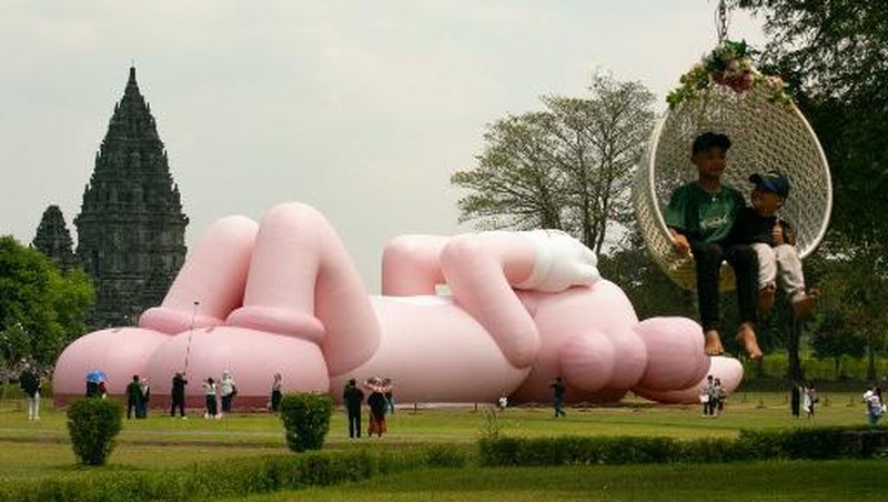 Instalasi seni berukuran raksasa yang dikenal sebagai KAWS, karya seniman Amerika Brian Donnelly terlihat menghiasi Candi Prambanan, Yogyakarta, Jawa Tengah. (DEVI RAHMAN / AFP)