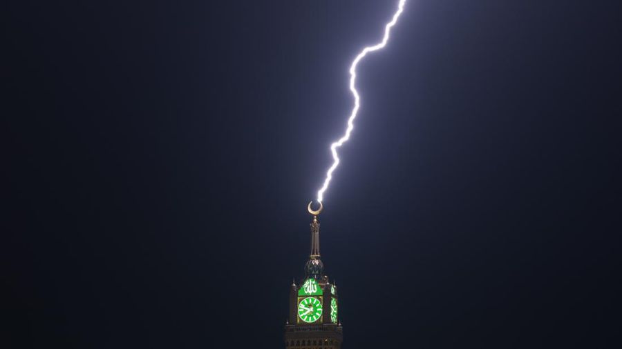 Sebuah gambar yang diambil pada 22 Agustus 2023 menunjukkan petir di atas menara jam Mekkah di Arab Saudi. Badai dahsyat menutup sekolah-sekolah pada tanggal 23 Agustus di wilayah Mekah di kerajaan gurun pasir, tempat Masjidil Haram berada, yang dilanda hujan lebat dan angin semalaman, kata para saksi mata. (Hammad Al-Huthali / AFP)