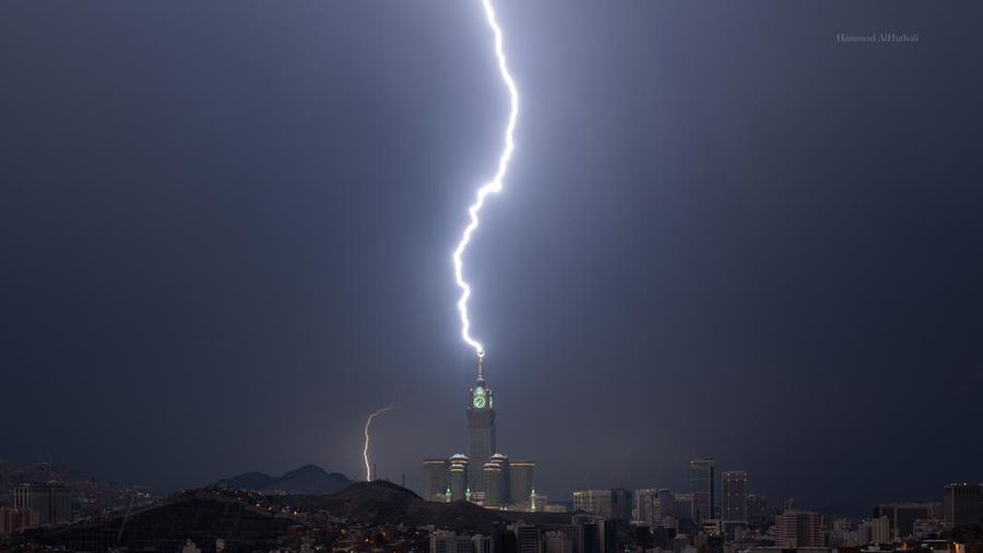 Sebuah gambar yang diambil pada 22 Agustus 2023 menunjukkan petir di atas menara jam Mekkah di Arab Saudi. Badai dahsyat menutup sekolah-sekolah pada tanggal 23 Agustus di wilayah Mekah di kerajaan gurun pasir, tempat Masjidil Haram berada, yang dilanda hujan lebat dan angin semalaman, kata para saksi mata. (Hammad Al-Huthali / AFP)