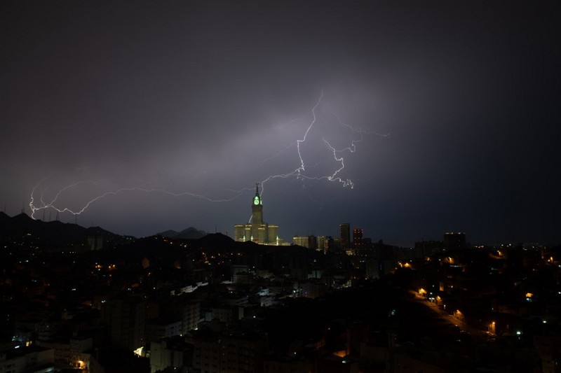 Sebuah gambar yang diambil pada 22 Agustus 2023 menunjukkan petir di atas menara jam Mekkah di Arab Saudi. Badai dahsyat menutup sekolah-sekolah pada tanggal 23 Agustus di wilayah Mekah di kerajaan gurun pasir, tempat Masjidil Haram berada, yang dilanda hujan lebat dan angin semalaman, kata para saksi mata. (Hammad Al-Huthali / AFP)