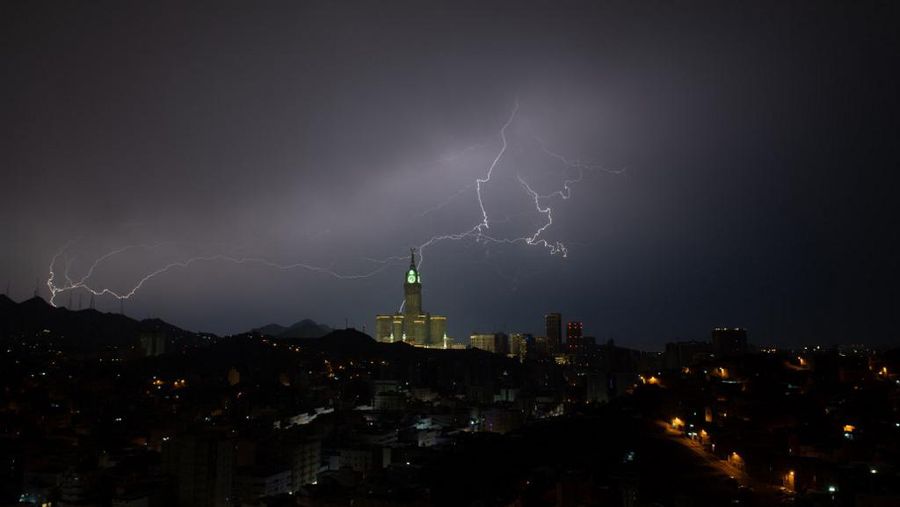 Sebuah gambar yang diambil pada 22 Agustus 2023 menunjukkan petir di atas menara jam Mekkah di Arab Saudi. Badai dahsyat menutup sekolah-sekolah pada tanggal 23 Agustus di wilayah Mekah di kerajaan gurun pasir, tempat Masjidil Haram berada, yang dilanda hujan lebat dan angin semalaman, kata para saksi mata. (Hammad Al-Huthali / AFP)