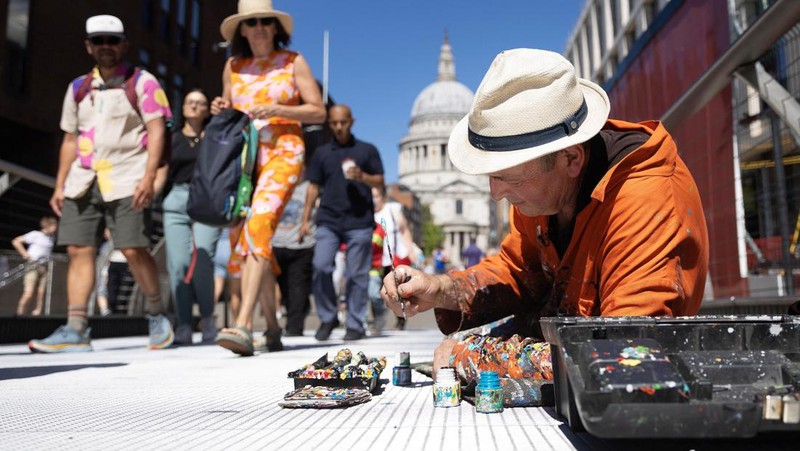 Ben Wilson, seniman, melukis di Millennium Bridge, London, Inggris, 21 Agustus 2023. (REUTERS/Anna Gordon)