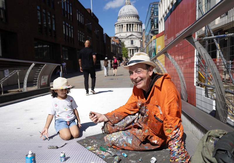 Ben Wilson, seniman, melukis di Millennium Bridge, London, Inggris, 21 Agustus 2023. (REUTERS/Anna Gordon)